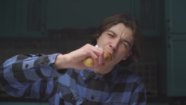 Νεαρός 20άρης που τρώει μπαγκέτα με αστείο τρόπο στην κουζίνα. Άντρας να σπάει ψωμί κοιτώντας την κάμερα και χαμογελώντας. Αστείο φαγητό.. — Αρχείο Βίντεο