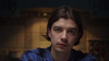 20 'li yaşların genç erkek portresi, karanlık odada yavaş çekimde kameraya bakıyor. Duygusuz, mavi gömlekli adam.. 