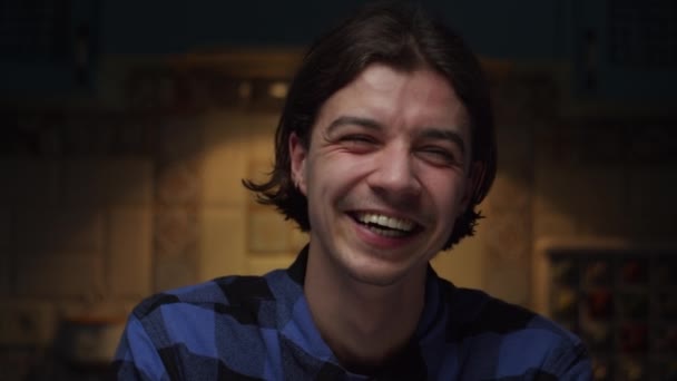 Close up of young 20s man portrait laughing looking at camera in dark room in slow motion. Good mood on mans face. — Stock Video