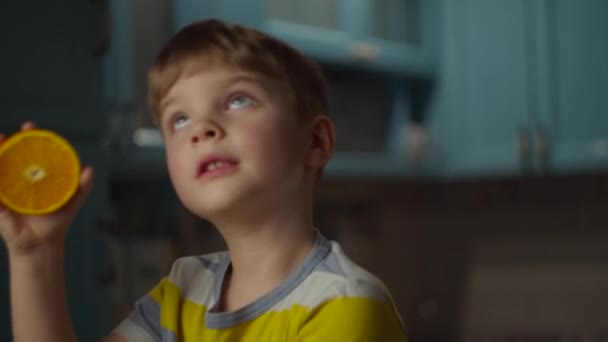 Garçon d'âge préscolaire jouant avec deux moitiés de fruits orange dans les mains à la maison. Enfant s'amuser avec des fruits orange au ralenti . — Video