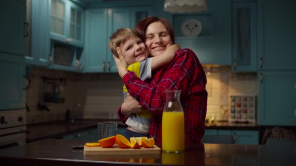 Žena nalévá pomerančový džus do sklenice pro chlapce. Mladí třicátníci, matka a syn si užívají rodinného času v kuchyni. Dítě pije ovocný nápoj s neplastovou slámou. — Stock video
