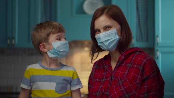 Young 30s mother and boy in medical masks looking at camera. Family in medical masks at home in self isolation from virus. Stop epidemic. — Stock Video