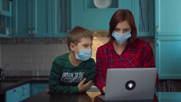 30 років мати і хлопчик в медичних масках дивляться на екран ноутбука і розмовляють онлайн з родичами, вітаючи махаючи руками. Сім'я в медичних масках вдома в самоізоляції від вірусу. Зупинити епідемію . — стокове відео