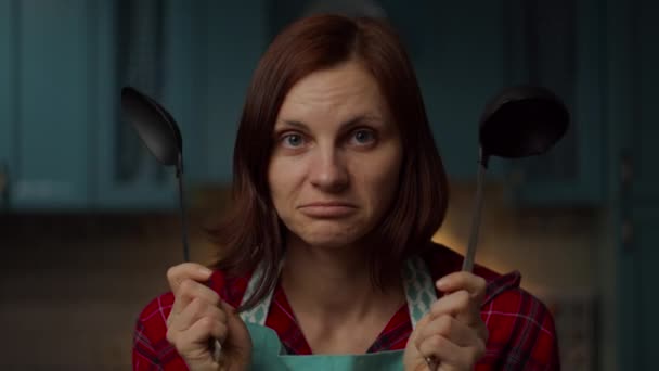 慌乱的30多岁的年轻女人手里拿着厨房用具犹豫地摇着头。女人不知道如何手拿着勺子和勺子做饭。靠近点. — 图库视频影像