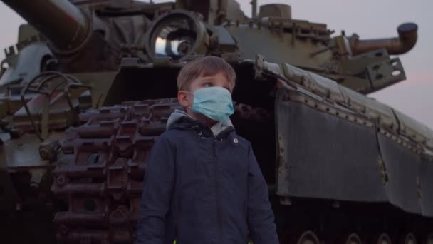 Pojke i medicinsk skyddsmask står vid militärmaskin under pandemiskt utbrott av coronavirus COVID-19 och tittar runt. Karantän nationella nöd- och undantagsbestämmelser för bekämpning av coronavirus. — Stockvideo