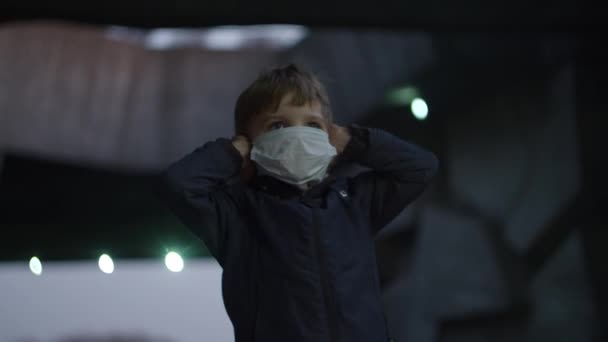 Αγόρι με ιατρική προστατευτική μάσκα στέκεται στο καταφύγιο κατά τη διάρκεια πανδημίας ξέσπασμα του coronavirus COVID-19 και φοβάται ρολόγια γύρω. Το παιδί κλείνει τα αυτιά λόγω της σειρήνας έκτακτης ανάγκης με κόκκινο φως σε εξωτερικούς χώρους. — Αρχείο Βίντεο