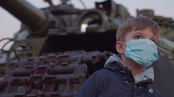 医療用保護マスクの少年は、コロナウイルスCOVID-19のパンデミック発生時に軍用機のそばに立ち、周りを見ています。コロナウイルスと戦うための検疫国家緊急および戒厳令. — ストック動画