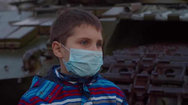 Шкільний хлопчик у медичній захисній масці стоїть на військовій машині під час пандемії коронавірусу COVID-19. Карантин надзвичайний і воєнний стан для боротьби з коронавірусом. Зачиніть. — стокове відео