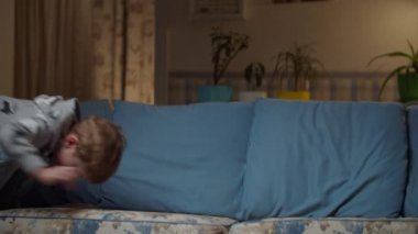 Kot pantolonlu çocuk oturma odasında takla atıyor. Çocuk kanepede akrobatik hareketler yapıyor. Sarışın çocuk, akşam odasındaki kanepede oynaşıyor..