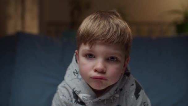 Portret van een jongen die thuis op de bank zit. Droevige kinderen gezicht kijken naar de camera in slow motion. — Stockvideo