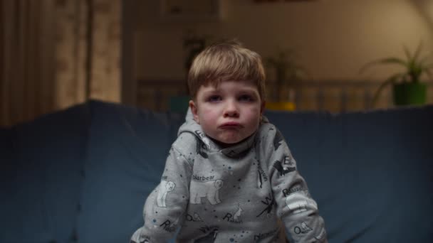 Portrét mladého rozrušeného chlapce sedícího doma na gauči. Smutné děti tváří v tvář pohledu na kameru ve zpomaleném filmu. — Stock video