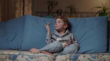 Sarışın anaokulu çocuğu, akşamları rahat koltukta dizlerinin üzerinde bir kase pirinçle. Çocuk yemek yemiyor. Kotlu çocuk TV karşısında öğle yemeği yiyor. 