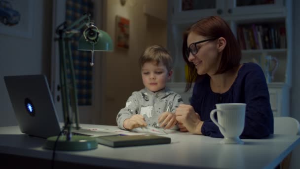 Joven madre de 30 años haciendo tarea en línea con el hijo preescolar en casa. Niño muestra respuesta correcta a la pantalla del ordenador portátil mientras estudia en línea. Proceso de educación en línea . — Vídeos de Stock