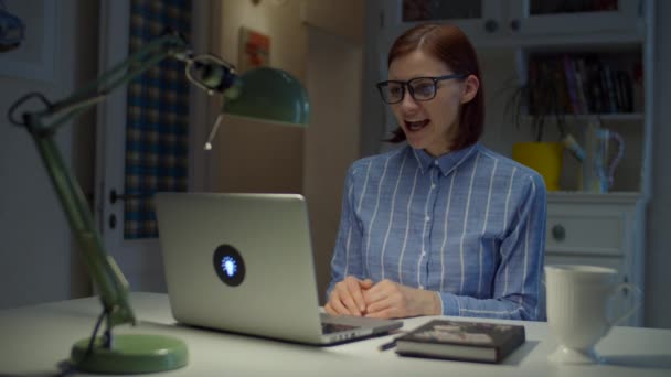 Professora sorridente dos anos 30 em óculos cumprimentando os alunos por videochamada e gesticulando emocionalmente olhando para o laptop em casa. Processo de educação online . — Vídeo de Stock