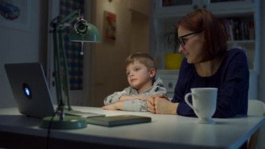 30 'lu yaşlardaki genç anne anaokulu çocuğuyla internette ödev yapıyor. Genç çocuk çevrimiçi çalışırken doğru cevap almak için el üstünde dizüstü bilgisayara doğru kalk. Çevrimiçi eğitim süreci. 