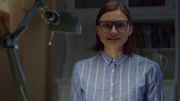 Sonriendo mujer de 30 años en gafas habla emocionalmente y gesticulando mirando a la cámara en casa. Proceso de educación en línea. Webcam vista del profesor hablando . — Vídeos de Stock