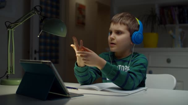 Uczennica w kolorowe słuchawki za pomocą tabletu do edukacji online w domu. Dzieciak lubi robić zadania domowe online, pokazując ręce do ekranu. — Wideo stockowe