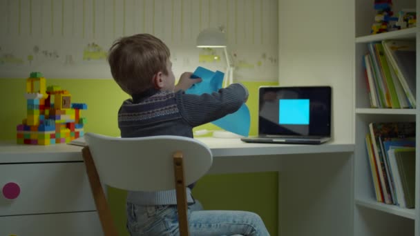Niño preescolar haciendo tarea de arte en línea. Niño corte azul forma cuadrada con tijeras sentado en el escritorio en la habitación de los niños en casa . — Vídeos de Stock