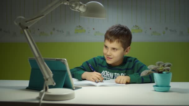 Colegial haciendo tarea en línea con la computadora de la tableta. Niño sentado en el escritorio y estudiando en línea en la habitación de los niños en casa . — Vídeos de Stock