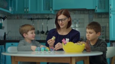 30 'ların annesi ve iki oğlu mavi mutfakta çikolatalı tavşan yiyor. Mutlu aile Paskalyayı renkli yumurtalar ve çikolatalı tavşanlarla kutluyor.. 