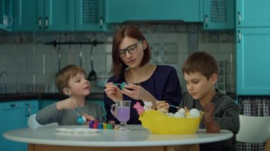 İki oğlu olan 30 'lu yaşlardaki genç anne mavi mutfağa Paskalya yumurtası çiziyor. Mutlu aile, renkli yumurta ve çikolatalı tavşanla Paskalya kutlamasına hazırlanıyor.. 