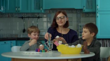 İki oğlu olan 30 'lu yaşlardaki genç anne mavi mutfağa Paskalya yumurtası çiziyor. Mutlu aile, renkli yumurta ve çikolatalı tavşanla Paskalya kutlamasına hazırlanıyor.. 