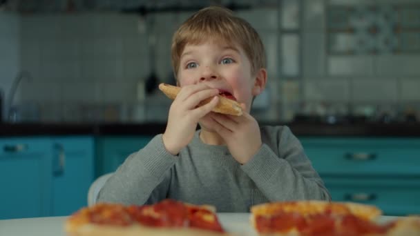 Een jongen die thuis pizza eet in de blauwe keuken. close-up van een kind genieten van Groot pizza in slow motion. — Stockvideo