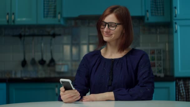 Jeune femme des années 30 dans les lunettes faisant la commande en ligne via l'application mobile sur la cuisine à la maison pendant la quarantaine. Femme reçoit sac de livraison à la maison . — Video