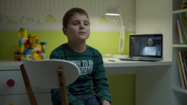 Bilgisayar ekranında bayan öğretmenle çevrimiçi derste masa başında oturan sıkıcı öğrenci. Evde internet eğitimi. Otistik çocuk çevrimiçi çalışıyor. 