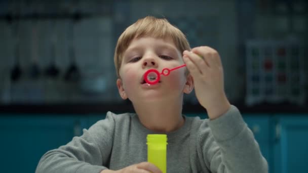 Garçon préscolaire blonde soufflant des bulles de savon assis à la maison sur la cuisine. Garçon jouer à la maison jeux seul au ralenti . — Video