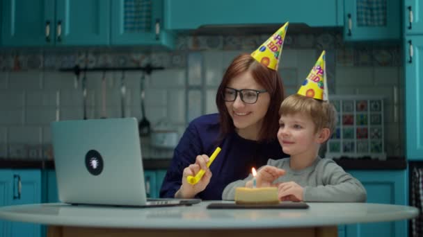 Joven mujer de 30 años y niño en sombreros de cumpleaños hablando con el ordenador portátil y agitando las manos. Familia feliz celebrar cumpleaños en línea en casa con vela en pedazo de pastel . — Vídeos de Stock