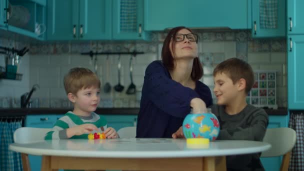 Joven madre de 30 años con dos niños jugando juegos de mesa en la cocina azul. Familia feliz divertirse con juegos de cartas en casa . — Vídeos de Stock