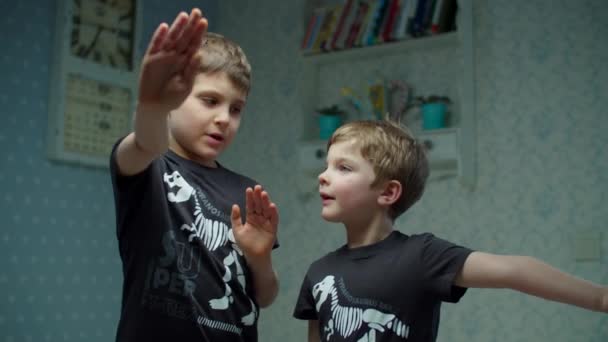 Dwóch braci w tych samych czarnych koszulkach śmiejących się i bawiących w domu. Chłopcy przybijający sobie piątkę w zwolnionym tempie. Uśmiechnięte rodzeństwo w domu. — Wideo stockowe