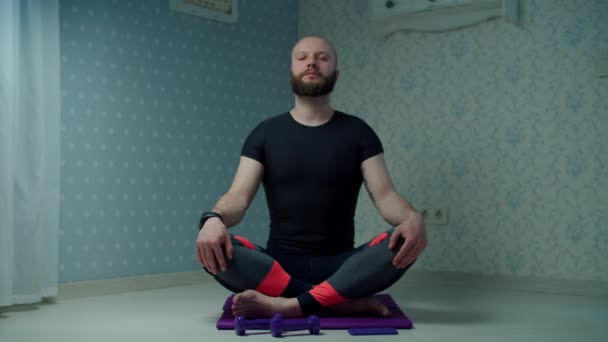 Barbudo hombre de 30 años en ropa deportiva haciendo yoga y ejercicios de meditación en la esterilla de fitness en casa. Hombre haciendo ejercicios de fitness en casa con pesas en cámara lenta . — Vídeos de Stock