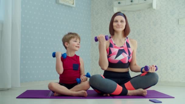 Preschooler boy making complex of sport exercises with young mother in sportswear at home. Happy family doing home fitness with dumbbells in slow motion. — Stock Video