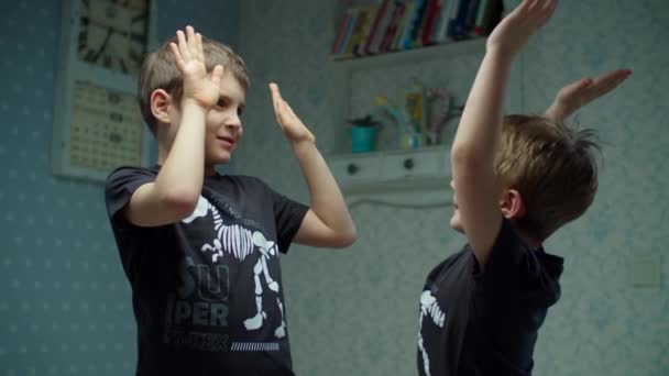 Δύο αδέρφια με ίδια μαύρα μπλουζάκια γελάνε και διασκεδάζουν στο σπίτι. Τα αγόρια να κολλάνε πέντε ο ένας στον άλλον σε αργή κίνηση. Χαμογελώντας αδέλφια στο σπίτι. — Αρχείο Βίντεο