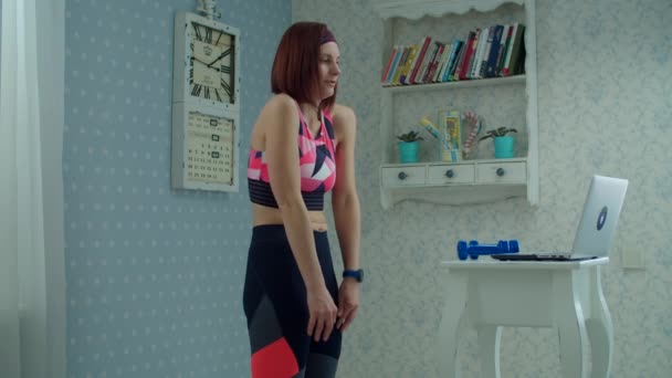 30s femme en vêtements de sport debout devant un ordinateur portable et faire des exercices de remise en forme à la maison. Femme faisant du sport avec des haltères à la maison au ralenti . — Video