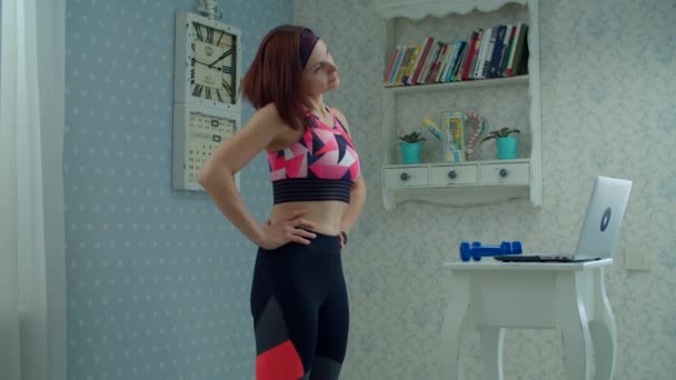 Donna 30s in abbigliamento sportivo in piedi di fronte al computer portatile e fare esercizi di fitness a casa. Donna che fa sport con i manubri a casa al rallentatore . — Video Stock