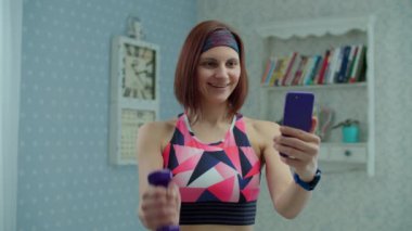 Spor kıyafetleri ve cep telefonu olan 30 'lu yaşlarda genç bir kadın evde ağır çekimde spor egzersizleri yapıyor.. 