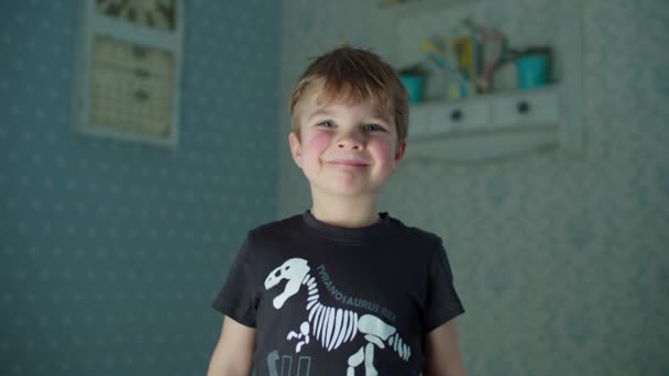 Niño sonriente de preescolar con camiseta negra de pie en la sala de estar y mirando a la cámara en cámara lenta. Retrato de un niño joven en casa . — Vídeos de Stock