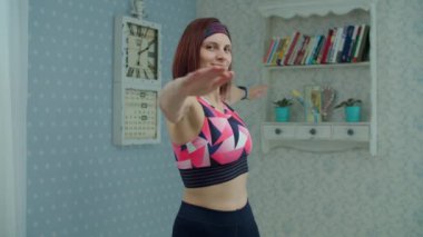 Spor giyimli 30 'lu yaşlardaki genç bir kadın evde spor egzersizleri yapıyor. Spor yapan kadın antrenmandan önce ısınıyor ve yavaş çekimde kameraya bakıyor.. 