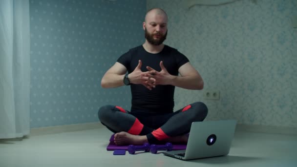 Bearded 30s man in sportswear making yoga and stretching exercises on fitness mat using online tutorial on laptop at home. Man doing home fitness exercises with dumbbells in slow motion. — Stock Video