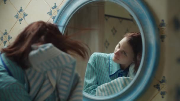 Молодая 30-летняя женщина в синей рубашке вытирает волосы полотенцем в синей ванной комнате дома. Зеркальное отражение женщины, делающей косметические процедуры дома. Закрыть — стоковое видео
