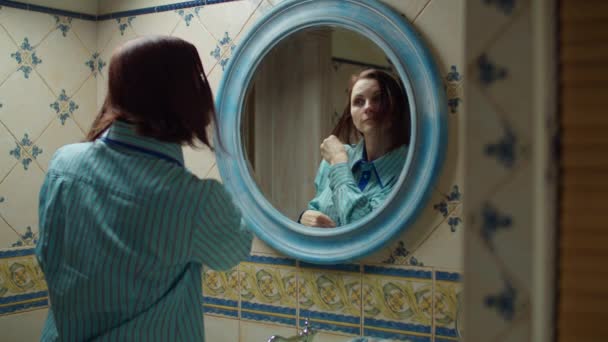 Mujer joven de 30 años con camisa azul cepillándose el pelo mojado en el baño azul en casa. Reflejo del espejo de la mujer haciendo procedimientos de belleza en casa . — Vídeo de stock