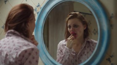 30 'lu yaşlardaki genç bir kadın aynanın önünde banyoda su içerek baş ağrısı hapı alıyor. Makyajı bozuk ve saçlarını bozuyor. Alkol, aynadaki yansıması olan tişörtlü sarhoş bir kadın. Kapat.