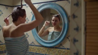 30 'lu yaşlardaki kadın saçını evde boyuyor ve ayna yansımasında dans ediyor. Saçları boyalı esmer kadın banyoda yavaş çekimde dans ediyor..