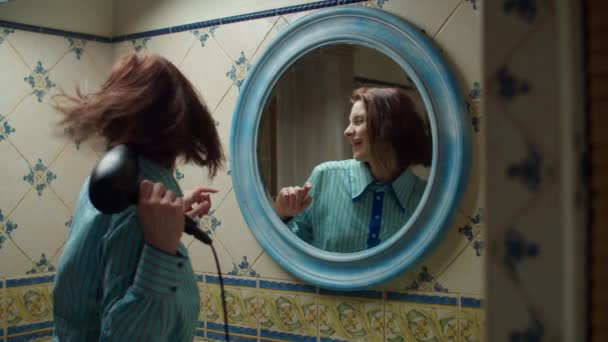 Mujer joven de 30 años con camisa azul secándose el pelo y bailando en el baño azul en casa. Reflejo espejo del canto femenino haciendo procedimientos de belleza en casa . — Vídeos de Stock