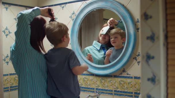 Młoda 30-letnia matka szczotkująca włosy swoich synów w łazience w domu. Szczęśliwa rodzina robi rutynę piękna w lustrze refleksji. — Wideo stockowe