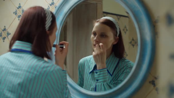Jonge dertiger jaren vrouw in blauw shirt die lippenstift aanbrengt op de lippen in de blauwe badkamer thuis. spiegelreflectie van dame doen make-up thuis. — Stockvideo