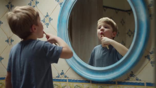 Szőke óvodás fiú, aki fogat mos otthon a fürdőszobában. Tükrözése gyerek fogkefével a kezében, hogy reggeli rutin — Stock videók
